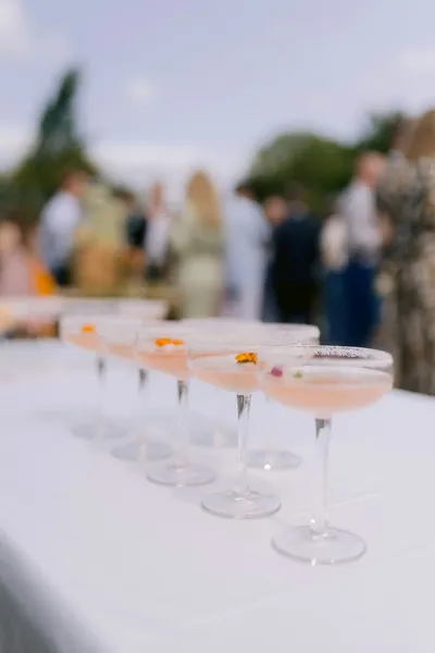 A row of pink cocktails in coupe glasses at an outdoor celebration