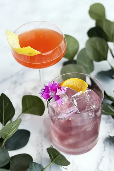 Two cocktails with fresh flower garnishes on a marble table
