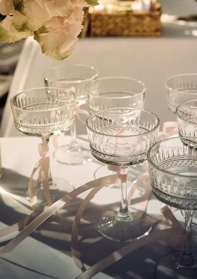 Coupe glasses tied with blush ribbons on a reception table